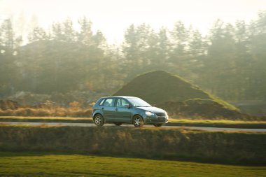 Siyah araba boş köy yolunda ilerliyor.