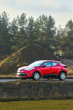 Kırmızı araba doğa arka planında yolda ilerliyor.