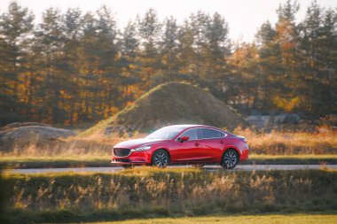 Kırmızı sedan güneşli kırsal alanda sürüyor.