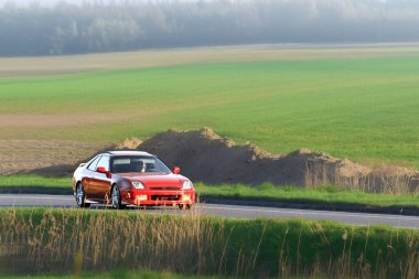 Kırsal kesime park edilmiş üstü açık kırmızı bir araba.