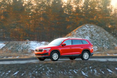 Şık kırmızı araç manzaralı bir kırsalda ilerliyor.