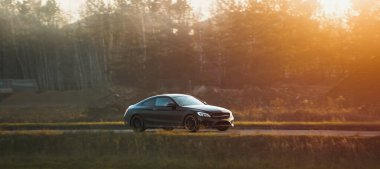 Tarz sahibi siyah bir sedan taşrada sürüyor.