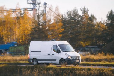 Kırsal yolda beyaz minibüs sürüyor.