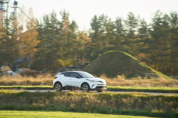 Beyaz hatchback sanayi bölgesini ve tarlaları geçiyor