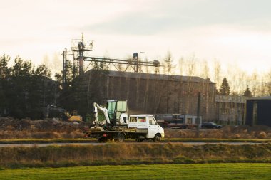 Sarı kamyon yolda inşaat makineleri taşıyor.