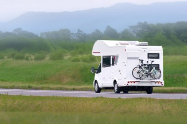 Manzaralı yolda bisikletli beyaz bir karavan.