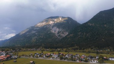 İlkbaharda dramatik bulutlu gökyüzünün altında karla kaplanmış görkemli Bavyera Alpleri