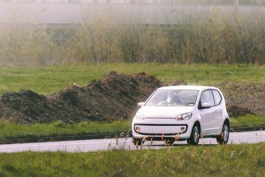 Asfalt yolda ilerleyen beyaz hatchback