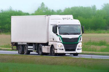 Kırsal yolda beyaz kargo kamyonu sürüyor.