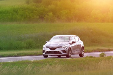 Şehir arabası hatchback yeşil tarlaları geçiyor.