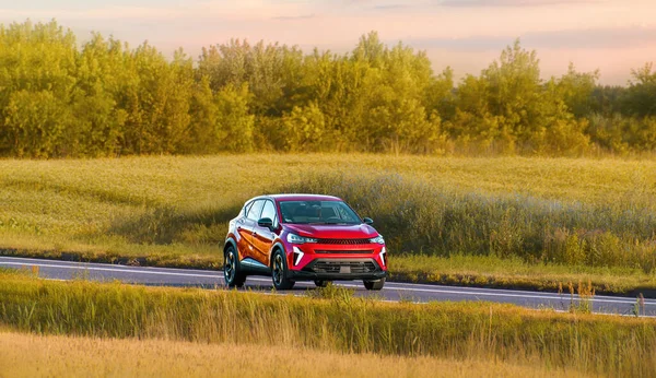 Melez araç manzaralı bir kırsal yolda ilerliyor.