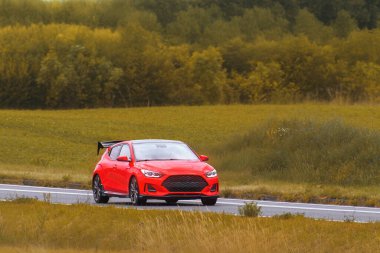 Parlak kırmızı spor araba açık asfaltta sürüyor.