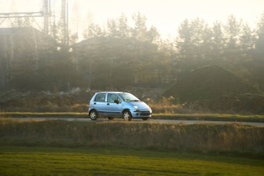Güneşli bir otoyolda küçük bir araç sürüyor.