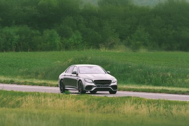 Açık yolda parlak yeni bir otomobil sürüyor.