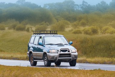 Modern bir arazi aracı huzurlu bir kırsalda ilerliyor.