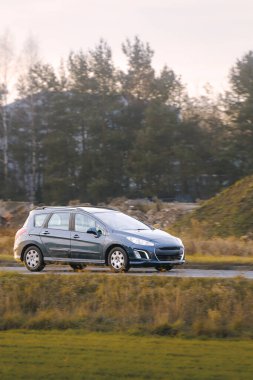 Parlak sonbahar yeşillikleri ve ormanlarla çevrili asfalt bir köy yolunda hızla ilerleyen bir SUV.