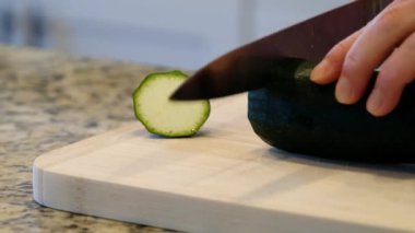Ev aşçısı, tahta bir tahtada çiğ kabak kesmek için bıçak kullanıyor. Kabaktan mermileri kesen bıçağı kapat..