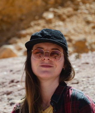 Beyzbol şapkalı, güneş gözlüklü, hippi gömlekli, dağların arkasında poz veren güzel bir kız.