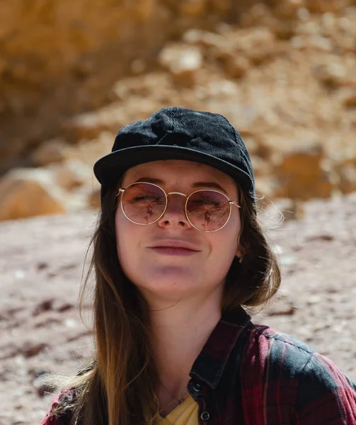 Beyzbol şapkalı, güneş gözlüklü, hippi gömlekli, dağların arkasında poz veren güzel bir kız.