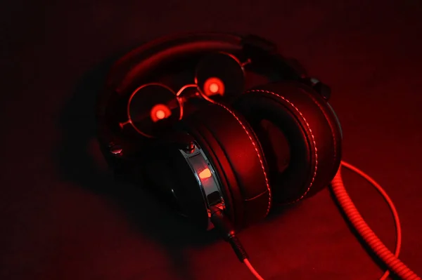 Stora DJ hörlurar med en röd kabel ligger på bordet tillsammans med runda solglasögon och belyses av ett rött ljus — Stockfoto