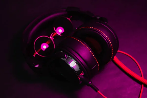 Stora DJ hörlurar med en röd kabel ligger på bordet tillsammans med runda solglasögon och belyses av ett lila ljus — Stockfoto