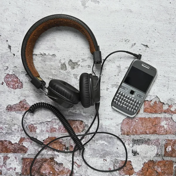 Fones de ouvido over-ear com um telefone de botão velho deitado em uma parede de tijolo flat lay — Fotografia de Stock