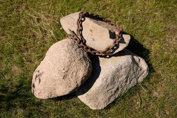 Como decoración en el parque en el prado hay tres grandes rocas y una cadena oxidada se encuentra en ellos — Foto de Stock