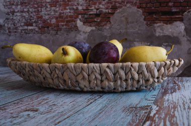 Meyve armutları ve eriklerle dolu sakin bir hayat hasır bir tabakta uzanır. Duvara karşı Provence tarzında tahtalarda duran bir tekne şeklinde.