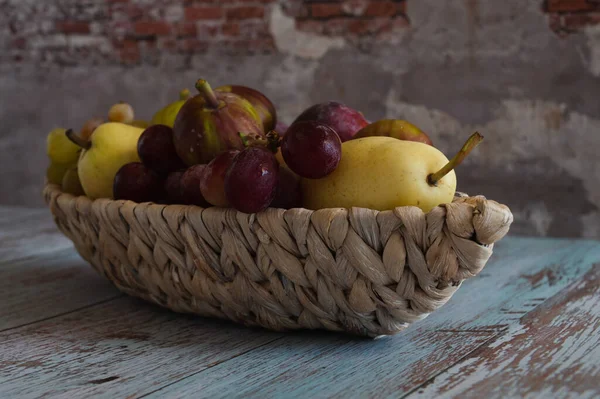 Stillleben mit Birnen und Pflaumen liegen auf einem Weidenteller in Form eines Bootes, das auf Brettern im Stil der Provence an der Wand steht. — Stockfoto