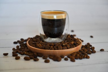 Bir cam bardak, kahverengi şekerli bir kasenin yanında, tahtadan bir tabağın içindeki kahve çekirdeklerinin üzerinde duruyor.