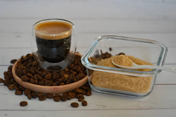 Ein Glas steht auf Kaffeebohnen in einem Holzteller neben einer Zuckerdose mit braunem Zucker — Stockfoto