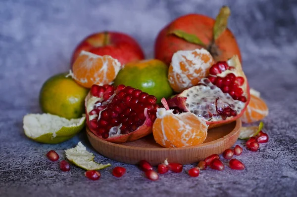 Ein Granatapfel, ganz und mit anderen Früchten in Stücke gebrochen, liegt auf einem Marmortisch — Stockfoto