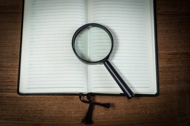 Boş defter büyüteç ile ahşap arka plan üzerinde açıldı.