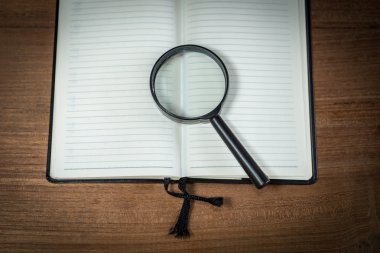 Boş defter büyüteç ile ahşap arka plan üzerinde açıldı.