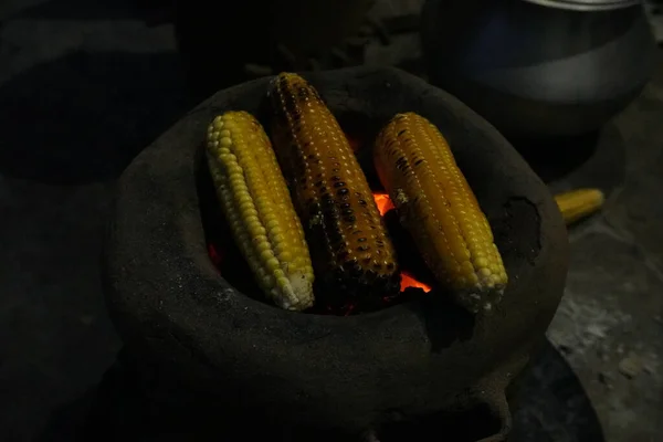 Koçandaki mısırlar geleneksel, kırsal bir pişirme düzeninde parlayan kırmızı közler üzerinde kızartılıyor..