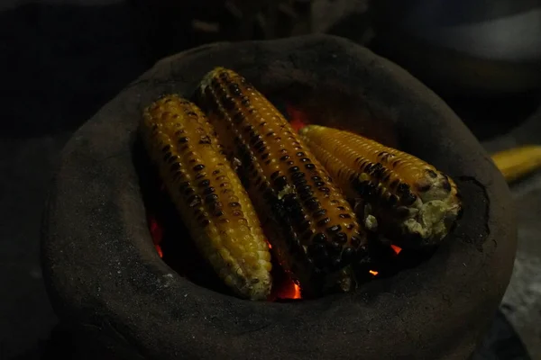 Koçandaki mısırlar geleneksel, kırsal bir pişirme düzeninde parlayan kırmızı közler üzerinde kızartılıyor..