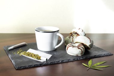 Tray with marijuana joints, fresh coffee and chocolate donuts with copy space top. Concept of marijuana and sweet food. clipart