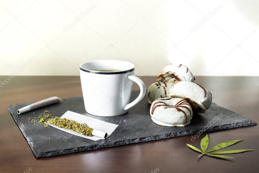 Tray with marijuana joints, fresh coffee and chocolate donuts with copy space top. Concept of marijuana and sweet food.