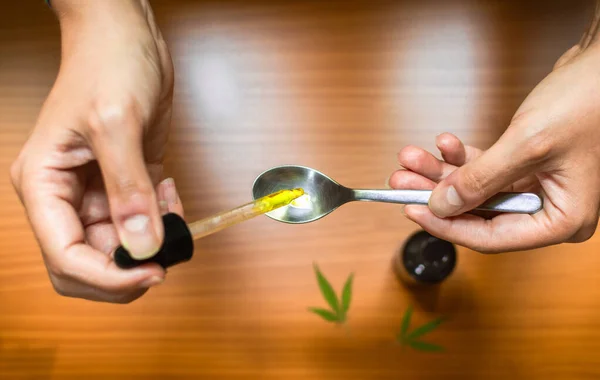Dozajı hesaplamak için bir kaşığa CBD yağı döken ellerin üst görüntüsü. Esrar yağı kullanmak.
