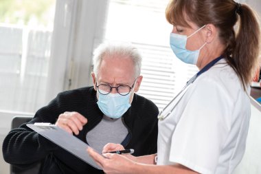 Korunaklı tıbbi maske takan kıdemli erkek hastayla görüşen kadın doktor; Coronavirus salgını sırasında tıbbi danışmanlık