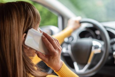 Araba kullanırken cep telefonuyla konuşan kadın.