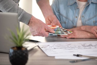 Yeni inşaat projesinin taslağı üzerinde çalışan ve renk örneği kullanan mimarlar
