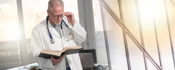 Ανώτερος Γιατρός Που Διαβάζει Ένα Βιβλίο Στην Κλινική Πολλαπλή Έκθεση — Φωτογραφία Αρχείου