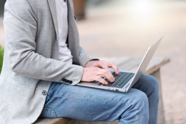 İş adamı dışarıda bir bankta oturuyor ve dizüstü bilgisayar kullanıyor. 