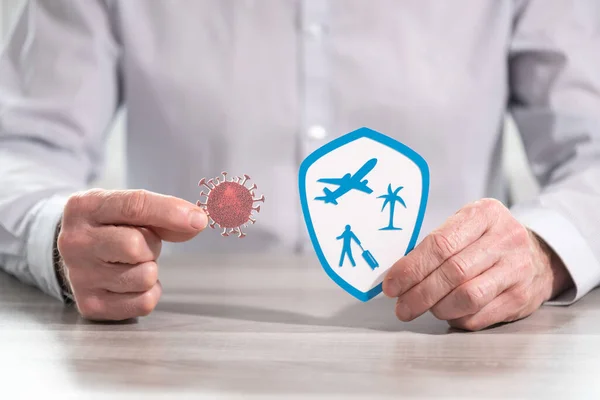 Man holding a virus and shield with travel symbols; concept of prevention and virus protection when traveling