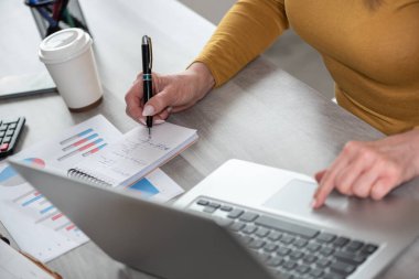 İş kadını dizüstü bilgisayar kullanırken not alıyor