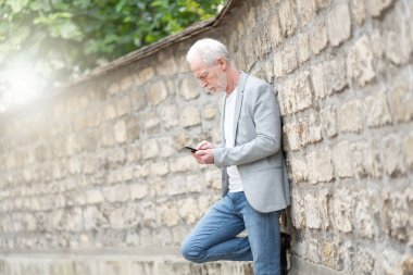 Olgun bir adam cep telefonunu açık havada kullanıyor.