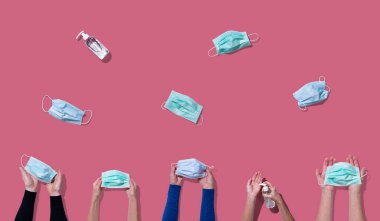 Yüz maskesi tutan ve koronavirüs önleyici önleyici önlem için dezenfektan kullanan eller açık mercan rengi arka planında; üst görünüm