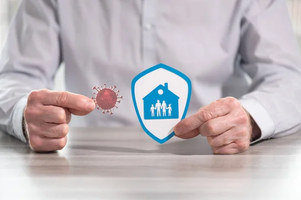 Man holding a virus and shield with a family at home; concept of family and home insurance during covid-19 outbreak