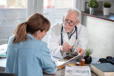 Başhekim, tıbbi ofisindeki kadın hastasına dijital tabletle ilgili raporlar gösteriyor.